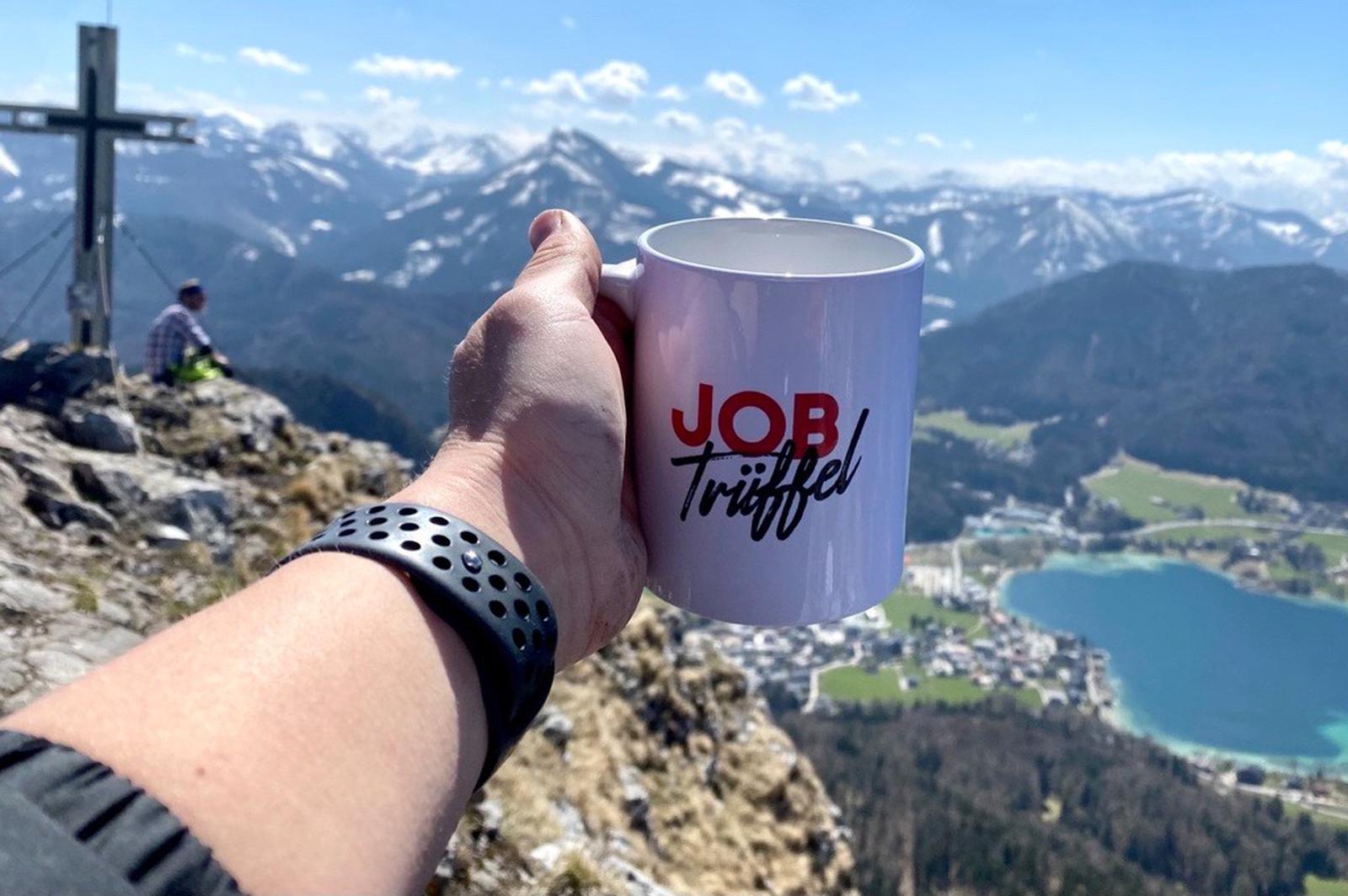 eine Tasse mit jobtrueffel logo vor dem Alpenpanorama